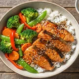 Grilled salmon rice bowl with avocado, edamame, cucumber and soy glaze on white plate